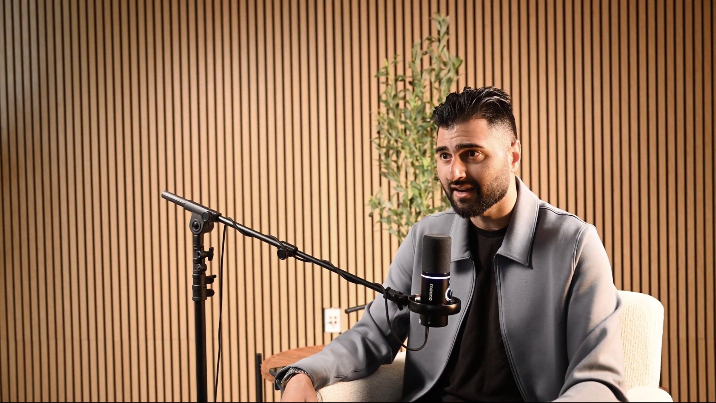 A man in a grey jacket talking into a boom microphone on the podcast set at Axeom Content Studio